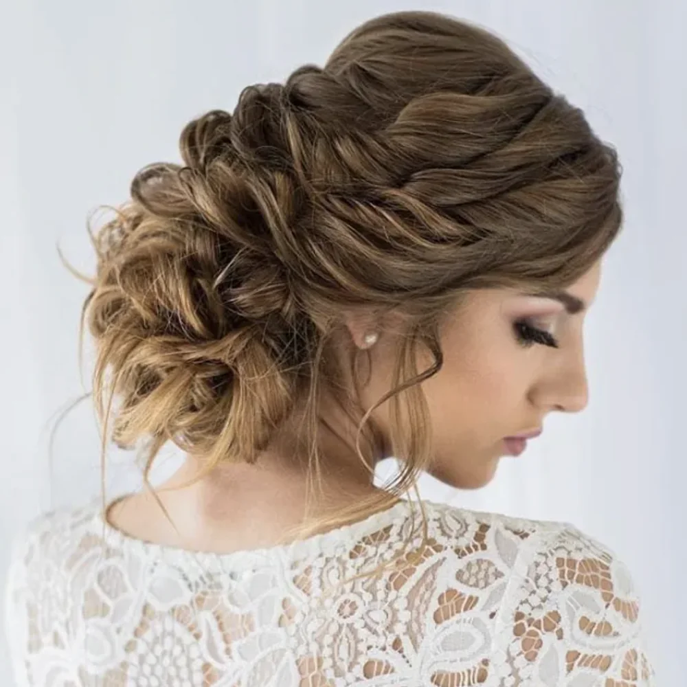 Soft braided bridal updo in brown hair with golden highlights, side view with a white lace top
