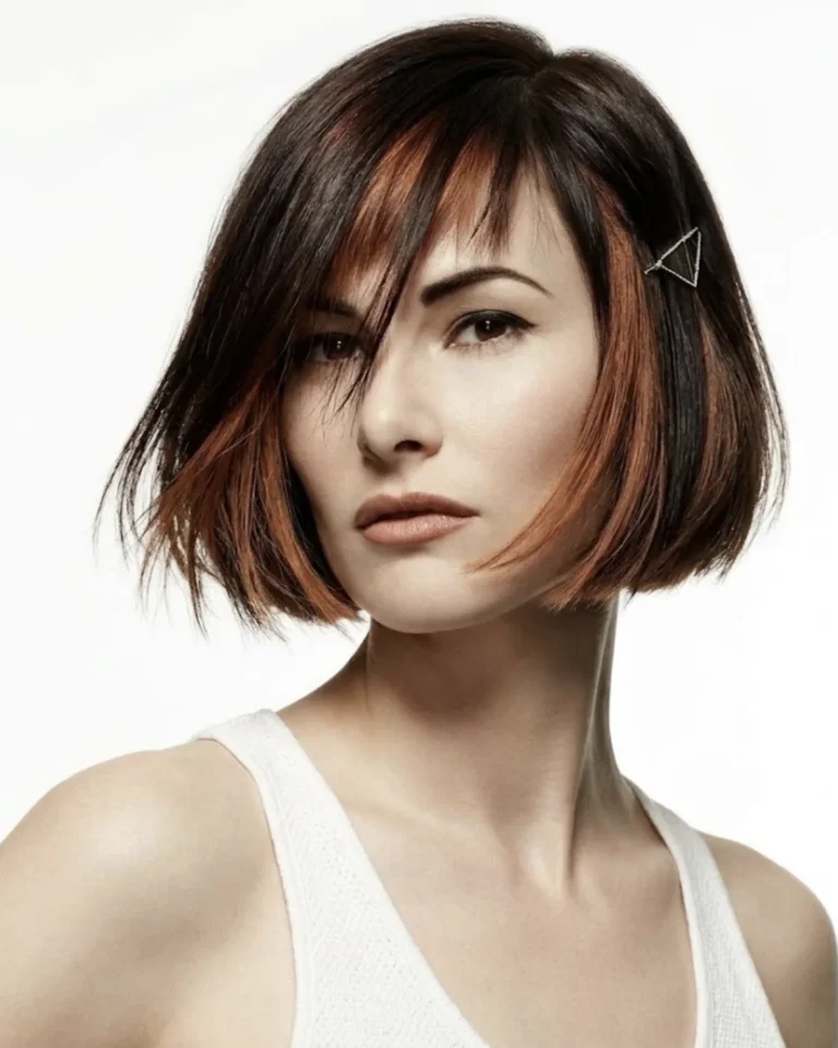 Chin-length precision bob with side-swept bangs and copper highlights in dark brown hair